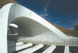 Top: aerial view, with oculus opening into the highway median. Above: view inside the arch, at path level.